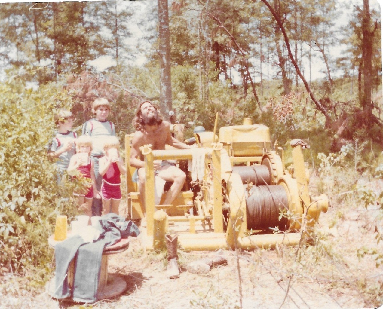 Curtis Gruetzmacher operating a cable winch with his children beside him, 1978