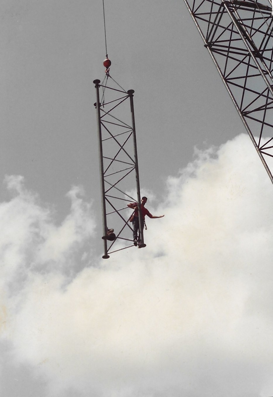 A worker riding a tower section being hoisted into the sky during a tower stack