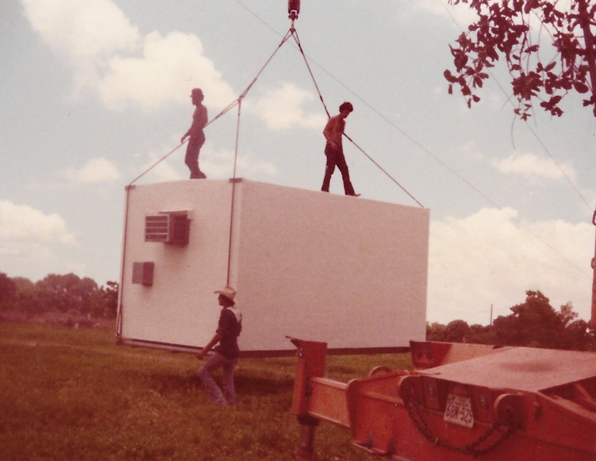Crew setting a communications equipment shelter with a crane